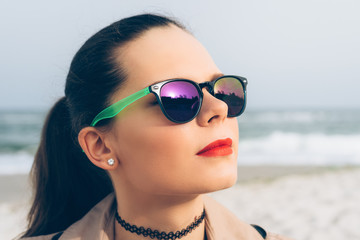 Fototapeta na wymiar Young woman in sunglasses looks at the sun on the beach in sprin
