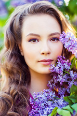 Naklejka premium Young beautiful girl near lilac bushes in blossom