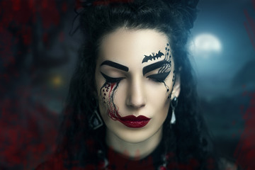 Young beautiful girl,woman, lady,witch, black bride, widow. Night cemetery, forest, background ,darkness, death. Bright fantasy makeup, red lips, blood, expressive eyebrows. Chic look for Halloween.