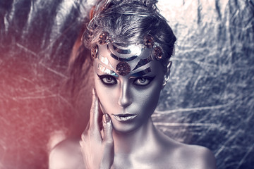 Portrait of beautiful young girl, woman, lady, hitman, killer, techno, future, progress. Ideal creative expressive makeup, silver skin, face, neck, shoulders, hand, arms. Stylish, bright, showy look.