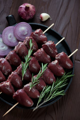 Frying pan with uncooked shish kebabs with turkey hearts