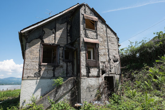 Altes Bauf&auml;lliges Haus am See mit H&uuml;gel im Hintergrund
