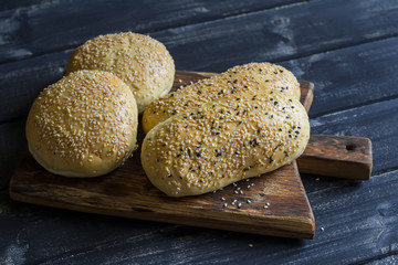 Hamburger and sandwich homemade buns on rustic wooden board on a dark background