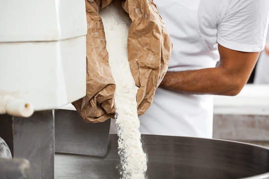 Midsection Of Baker Pouring Flour In Kneading Machine