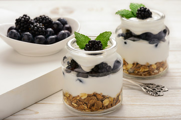 Healthy yogurt dessert with muesli, blackberries and  blueberries on white wooden table.