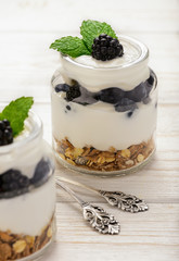 Healthy yogurt dessert with muesli, blackberries and  blueberries on white wooden table.