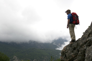 A man standing on a ledge in a rock face among clouds.