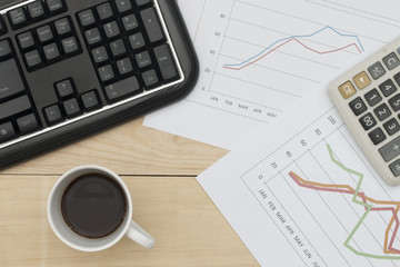 Workplace with keyboard, graph, calculator, and coffee on wood t