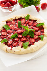 Homemade strawberry galette decorated mint leaves on white wooden background