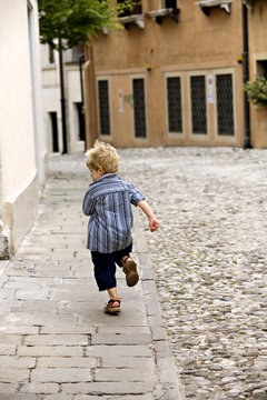 A very young boy running away from the photographer.