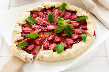 Homemade strawberry galette decorated mint leaves on white wooden background