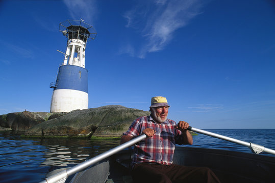 A man in a rowing-boat and a lighthouse on a rock, Sweden.