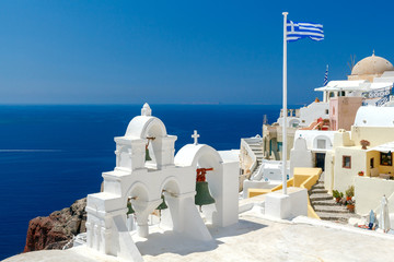 Fototapeta na wymiar White bell tower and Greek flag in Oia.