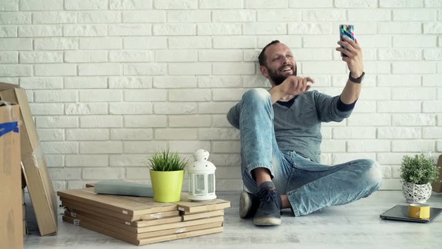 Man with glass of wine talking selfie photo with cellphone on floor at his new home
