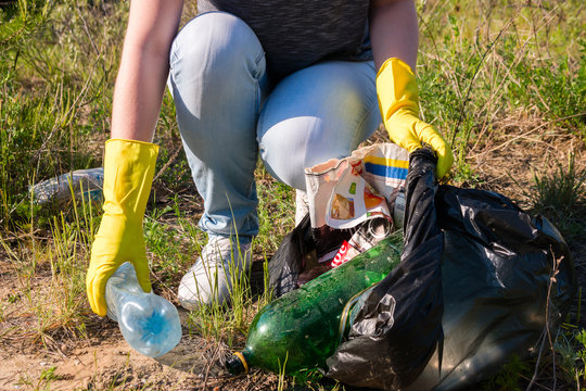 Volunteer girl in yellow gloves collects garbage selective focus