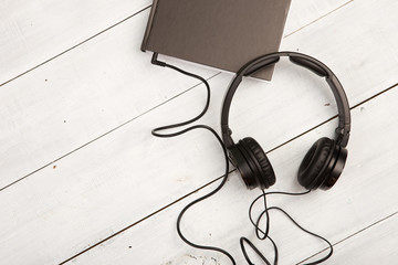 Audio book concept with black book and headphones on white wood