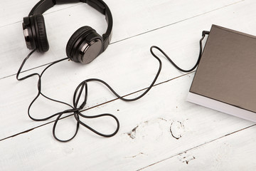 Audio book concept with black book and headphones on white wood
