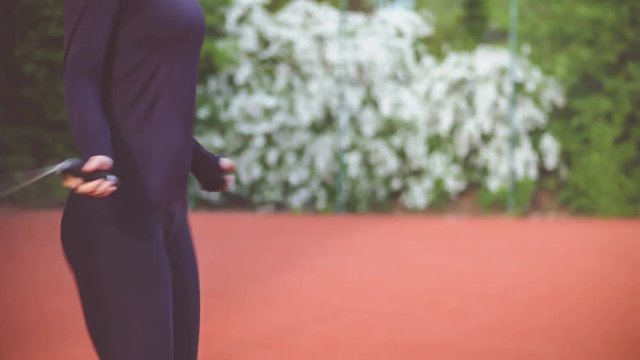 Close-up of hands an jumping women on the jump rope. Outdoor sports. Girl jumping on a skipping rope on sport court. Flower busch on background. 4K 3840 x 2160 ultra high definition footage