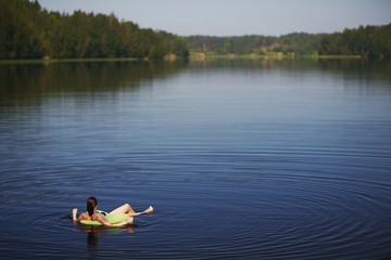 Fototapeta na wymiar relaxed young woman lying on inflatable ring in lake and admiring the stunning views. Away on a blurred background forest and sky. Top view .