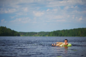 Fototapeta na wymiar relaxed young man lying on inflatable ring in lake and admiring the stunning views. Away on a blurred background forest and sky.