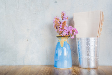 Pink flower in blue vase on a wooden table with cement wall back