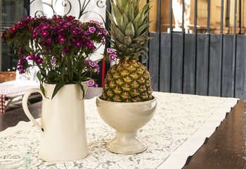 Fototapeta premium Jug with flowers and pineapple on table of street cafe