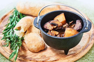 Ragout of veal with mushrooms, sauce demiglas in an iron pot and crusty bread on a wooden plate