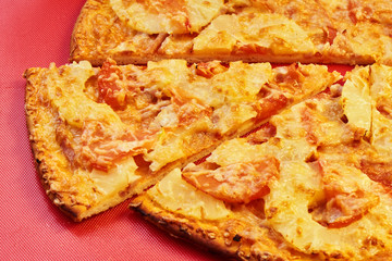 A slice of pizza with pineapple and ham baked with cheese is on the red surface