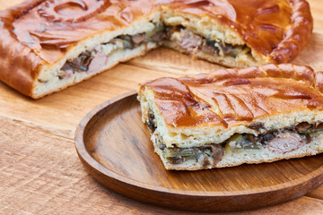 Slice of pie with chicken and mushrooms on wooden plate
