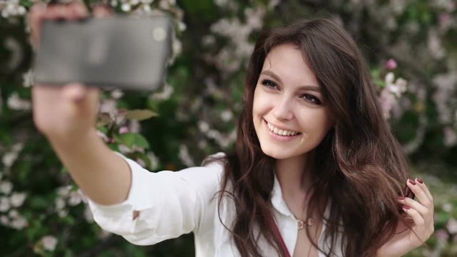 Happy woman taking selfie on tablet in the blooming garden.