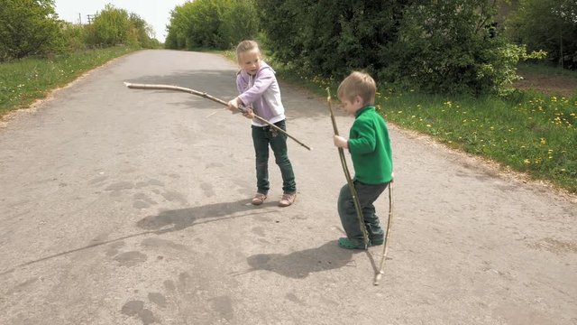 Happy children little girl and boy brother and sister play with bug beetle and rods on the road. Carefree childhood summer happiness and green environment education concept. 4K UHD video footage.