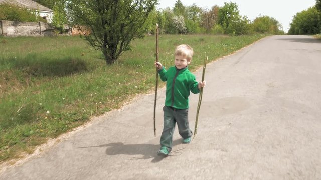 Happy cute little 3-5 years child boy plays outdoor game with rod and walks outdoor on road. Carefree childhood summer and happiness concept. 4K UHD video footage.