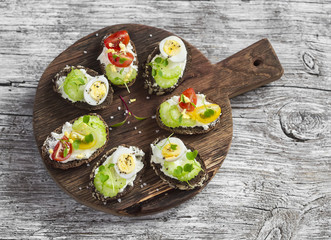 Sandwiches with soft cheese, quail eggs, cherry tomatoes and celery. Delicious healthy snack or Breakfast. On a wooden rustic board