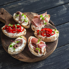 Sandwiches with goat cheese, anchovies, roasted peppers, ham on a wooden rustic board. Delicious snack or appetizer with wine