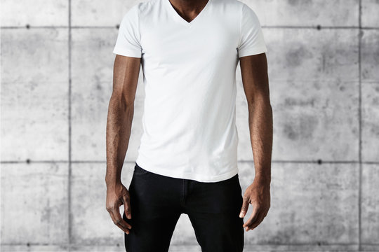 Cropped studio shot of dark skinned young male posing against white copy space wall wearing white T-shirt with copy space for your advertising content. T-shirt design and advertising concept.