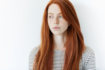 Close up shot of beautiful Caucasian woman with long red hair, wearing striped top, looking away...