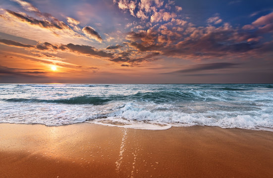 Fototapeta Colorful ocean beach sunrise with deep blue sky and sun rays.