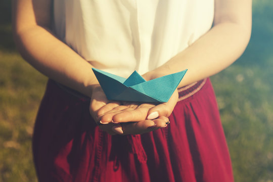 Female holding paper boat outdoors.