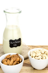 Bottle of homemade plant based milk and bowls with ingredients on wooden surface, and white background