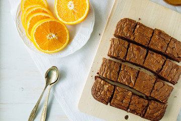 Chocolate brownie, orange and spoons on table