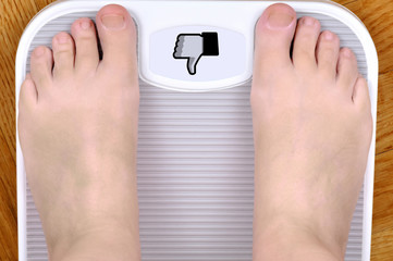 Barefoot person standing on the weight scale. The scale shows dislike sign       