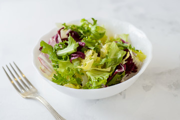 Mixed fresh vegetable salad (green iceberg lettuce, radicchio and frisee) in white bowl on a white background