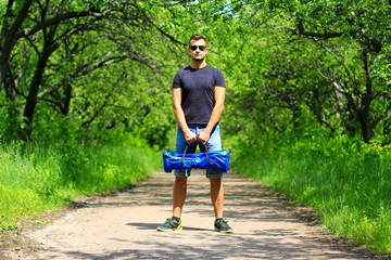 young fit man carrying a sports bag with hoverboard - personal portable eco transport, electrical scooter, gyro scooter, smart balance wheel