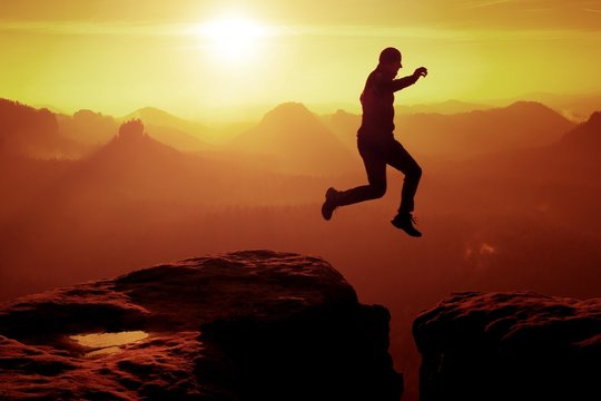 Young crazy man jump on mountain peak. Silhouette of jumping man