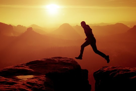 Young crazy man jump on mountain peak. Silhouette of jumping man