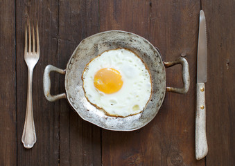 Fried egg in a old frying pan with fork and knife