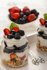 Healthy yogurt dessert with muesli, strawberries, blackberries and  blueberries on white wooden table.