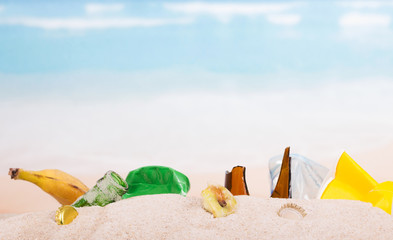 Leftovers, banana skins, plastic, glass bottles in  sand against  sea.