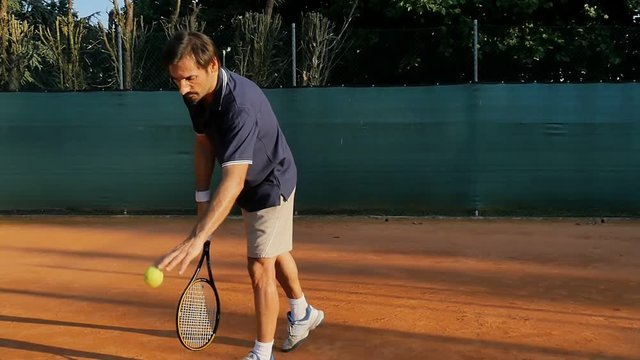 male tennis player serving ball slow motion on a red clay court crane shot