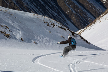 Man snowboarder snowboarding on fresh white snow on ski slope on Sunny winter day